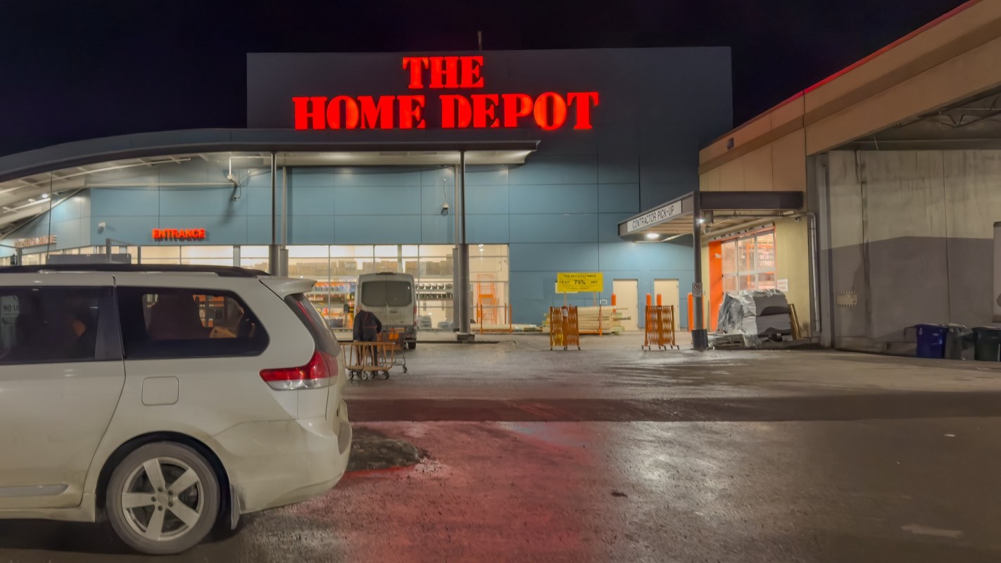 A Home Depot store entrance at night with a parked vehicle in the foreground.