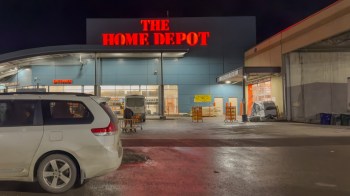 A Home Depot store entrance at night with a parked vehicle in the foreground.