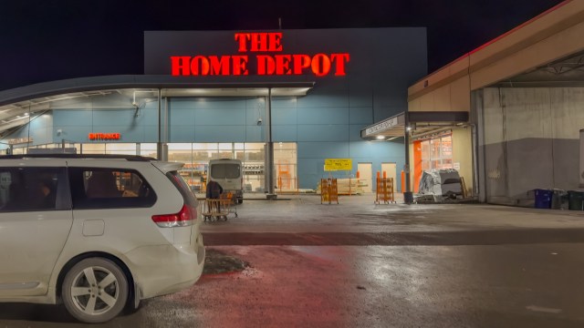 A Home Depot store entrance at night with a parked vehicle in the foreground.