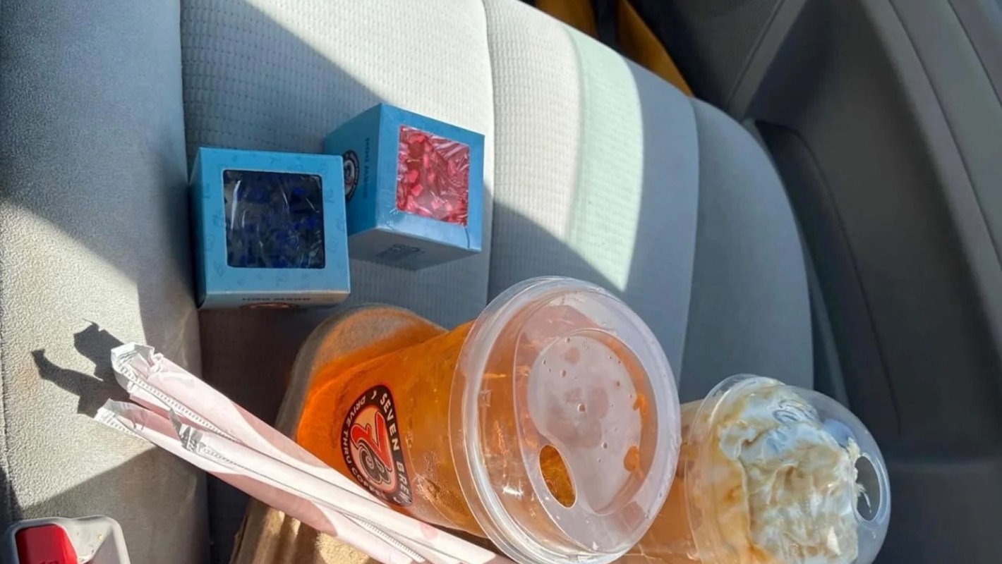 A beverage, a dessert drink with whipped cream, and two small boxes are on a car seat.