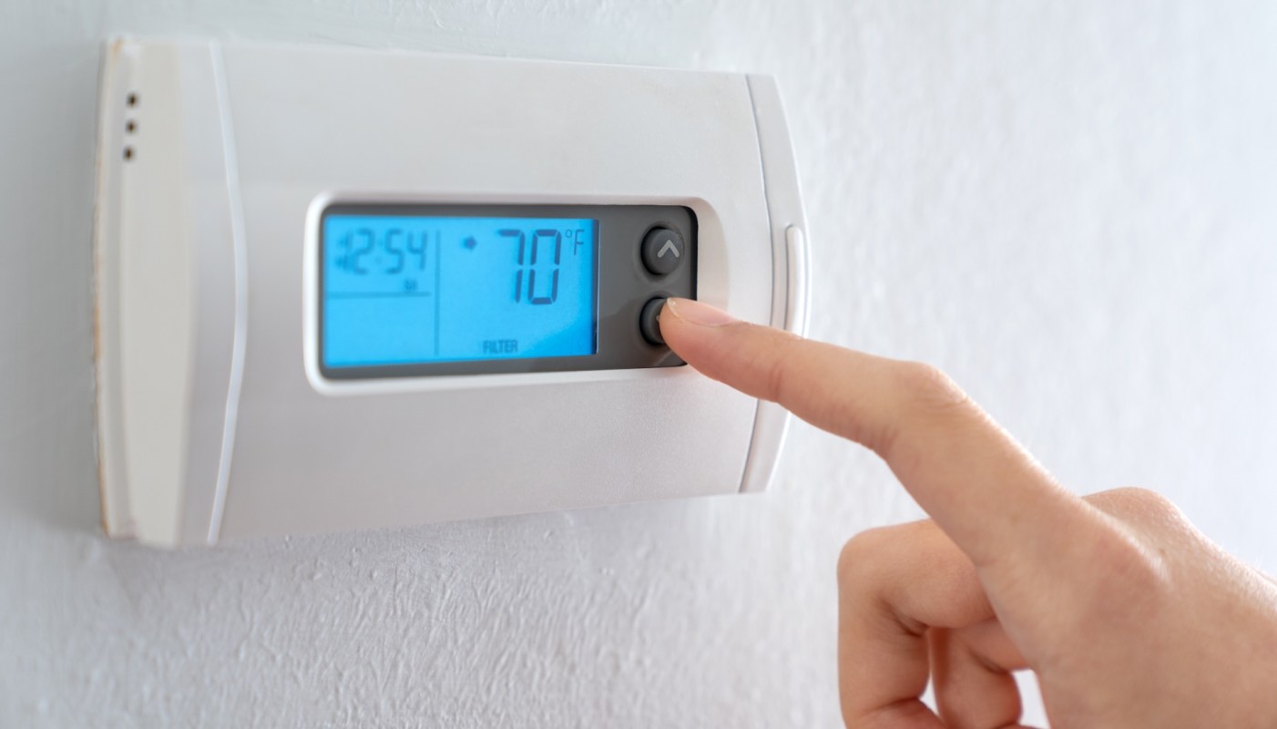 A hand adjusts a digital thermostat displaying the temperature at 70°F.