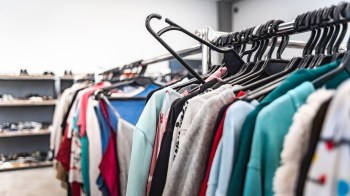 A clothing rack filled with various garments and a display of shoes in the background.