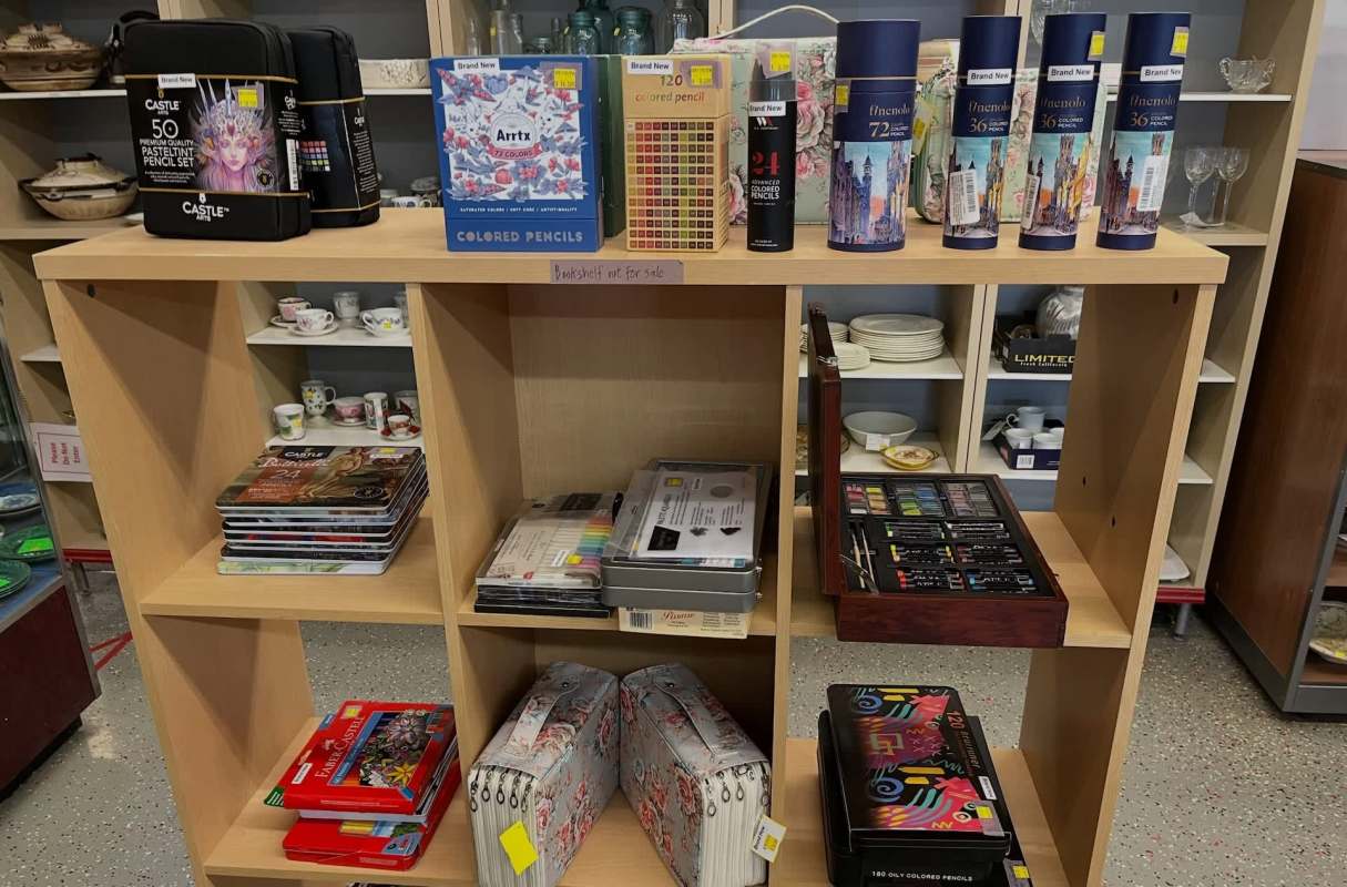 A shelf displaying various art supplies including colored pencils, sketchbooks, and tool sets.