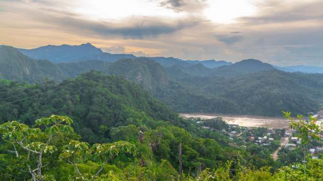 A panoramic view of lush green mountains and a river valley under a cloudy sky.