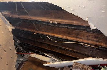 A view of exposed wooden beams and electrical wiring from a damaged ceiling.