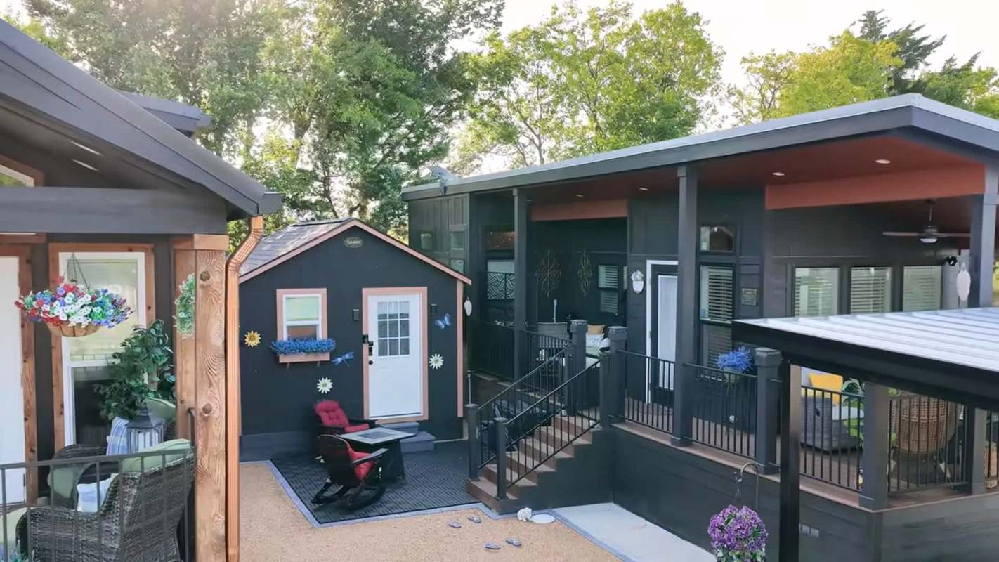 A modern house with a black exterior, a small shed, and a porch decorated with flowers and outdoor seating.