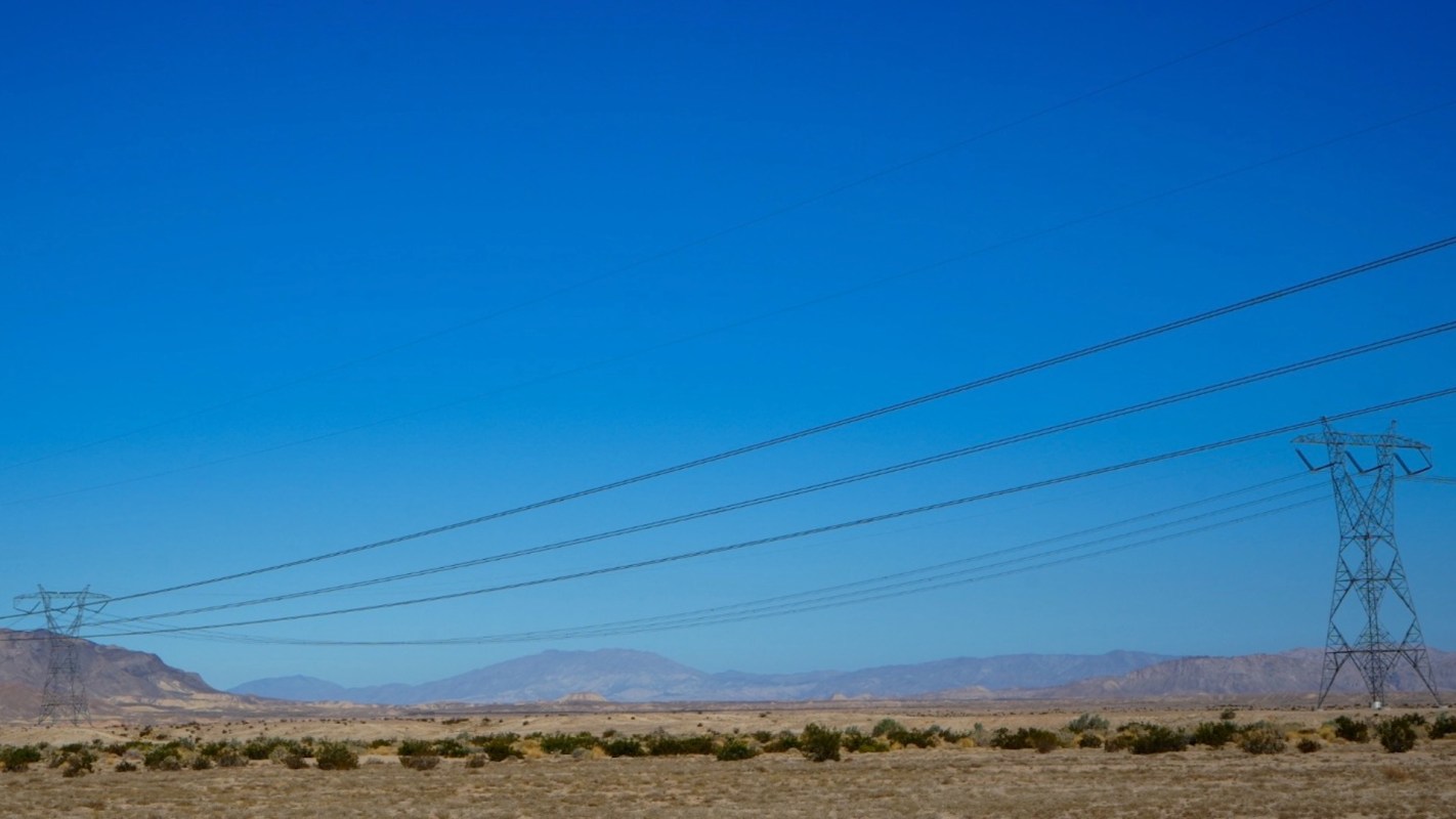 A vast landscape with power lines extending across a clear blue sky and distant mountains.