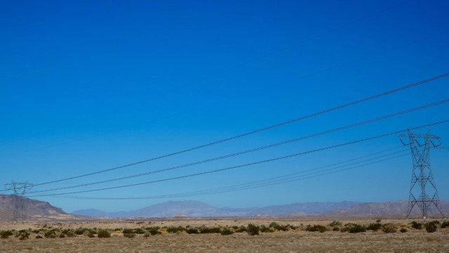 A vast landscape with power lines extending across a clear blue sky and distant mountains.