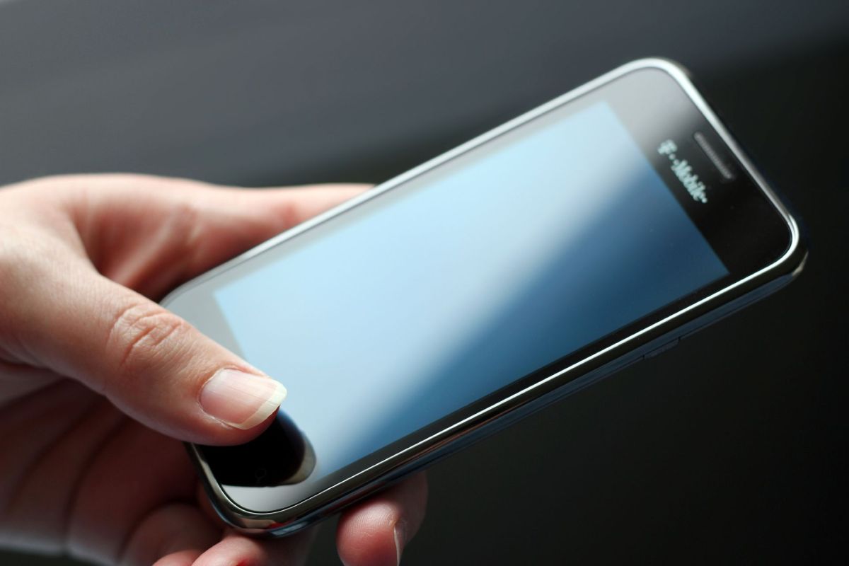 A person holds a black cell phone that has Tmobile written on it