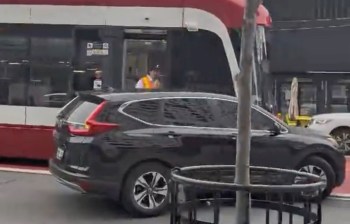 A black SUV is stopped near a red and white transit vehicle in an urban setting.