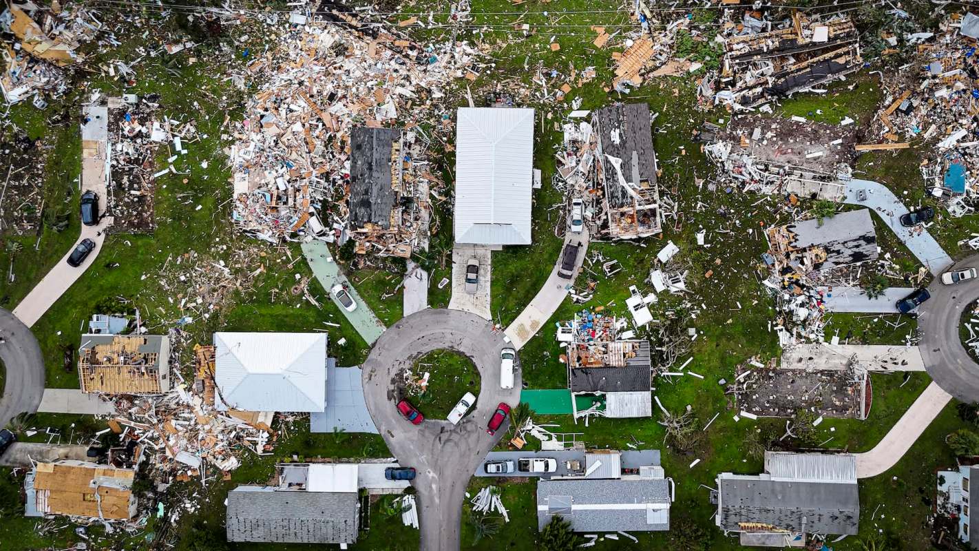 An aerial view of a neighborhood showing damaged homes and debris scattered across the ground.