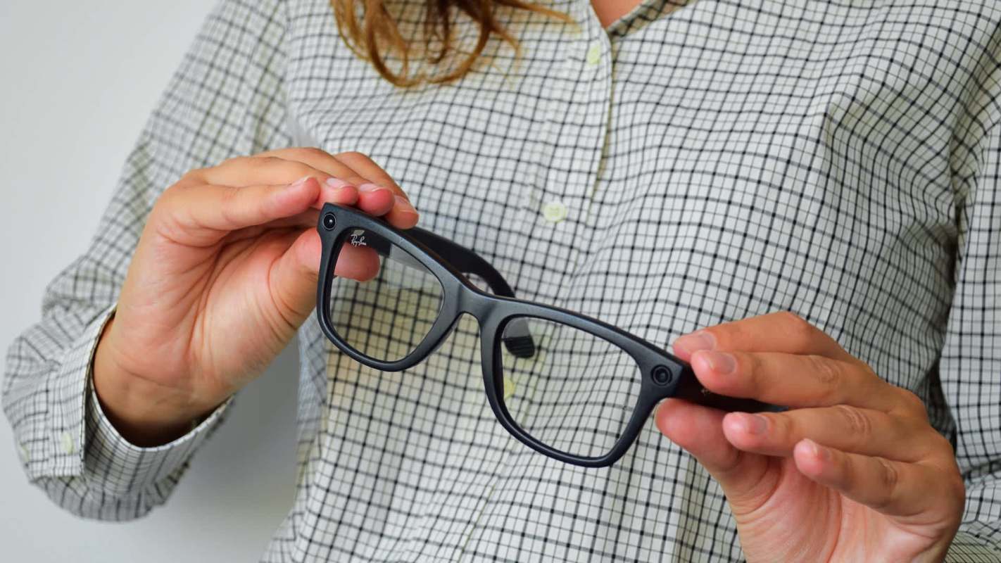 A person holding a pair of glasses with black frames.