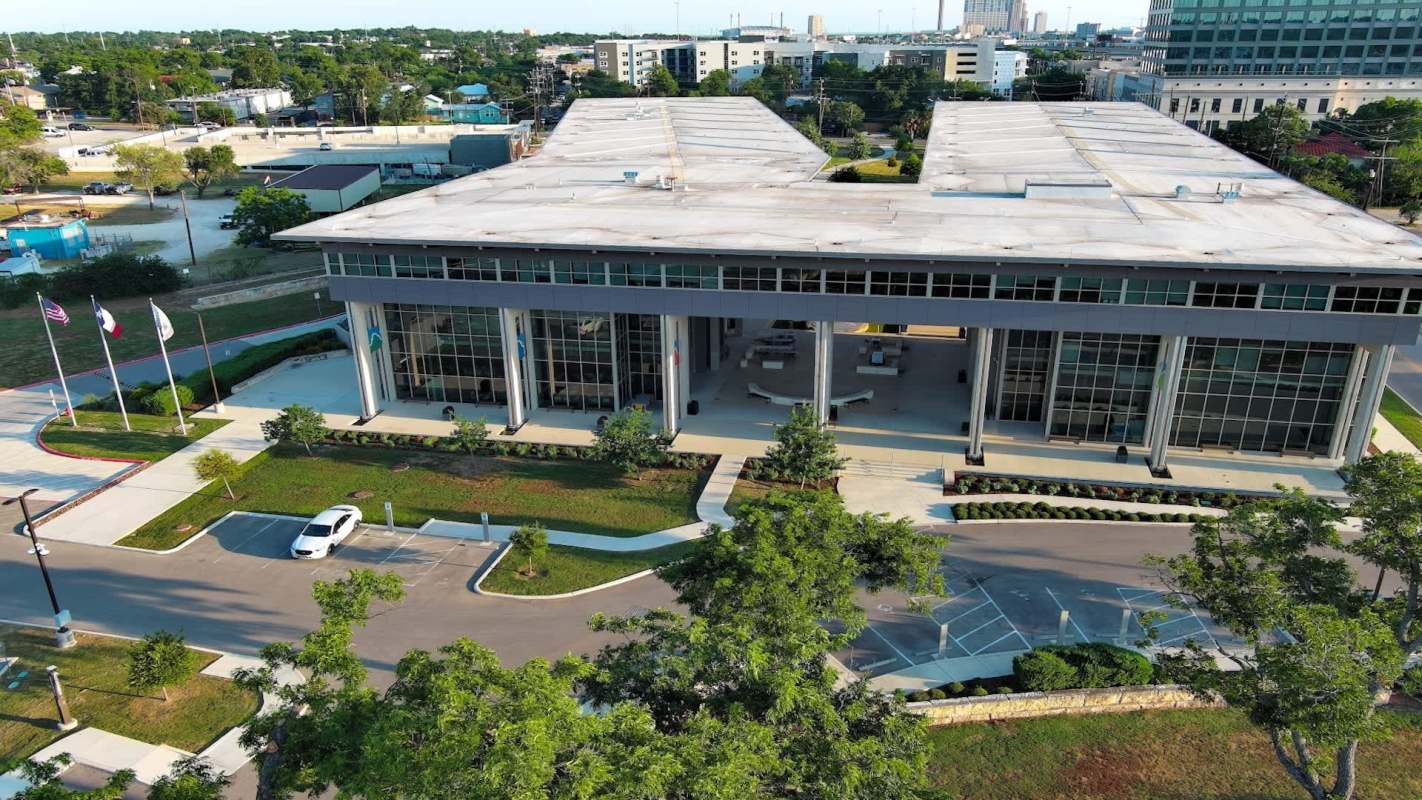 A modern building with large glass windows, surrounded by landscaped areas and flags.