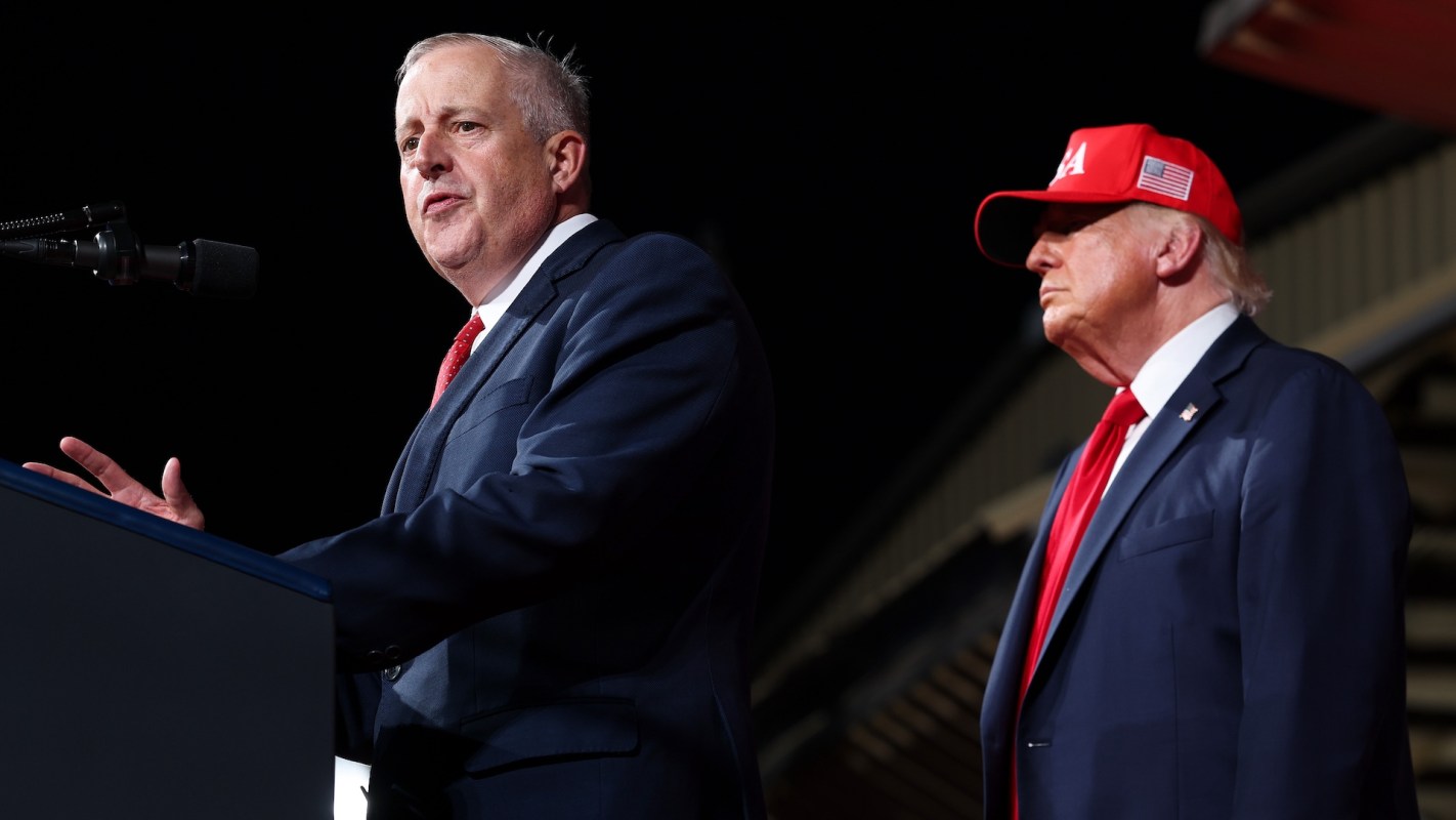 Michael Whatley speaks at a podium while President Donald Trump stands beside him.