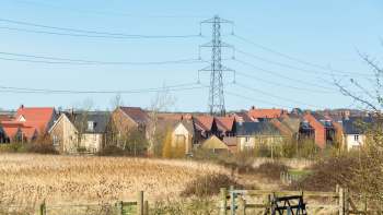A row of British houses with various roof styles and a power line overhead, set against a clear sky.