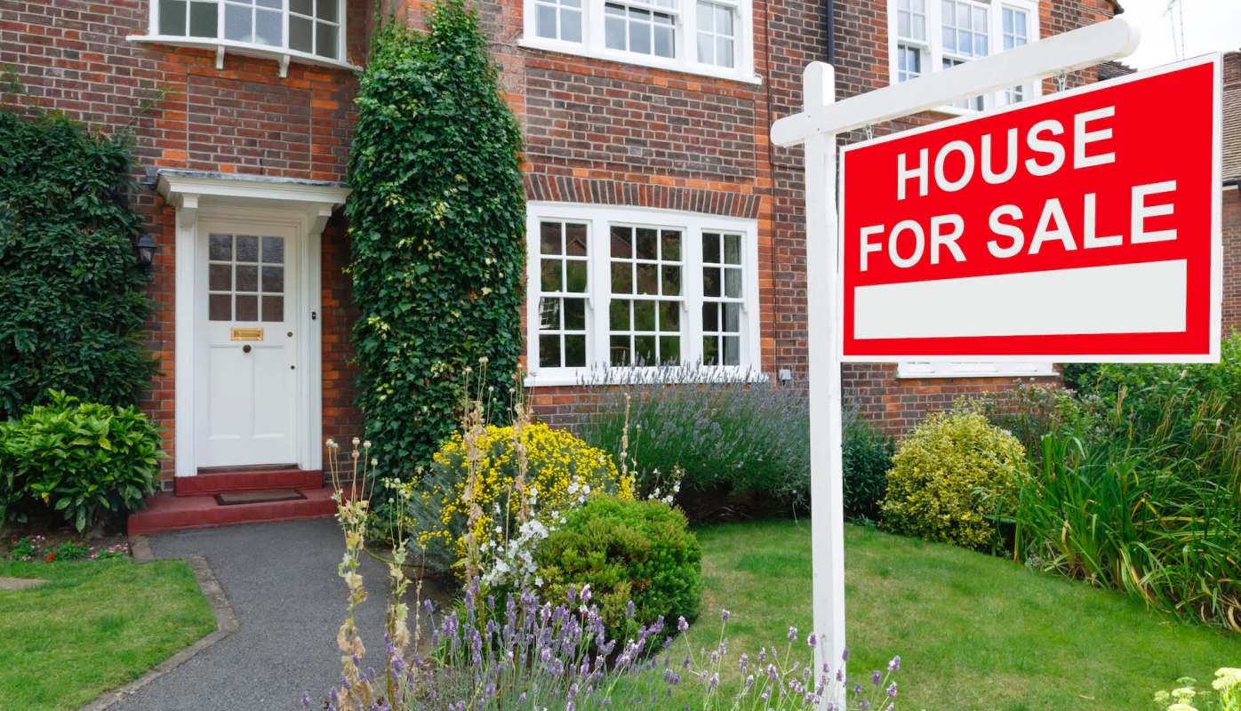 A brick house with a "For Sale" sign.