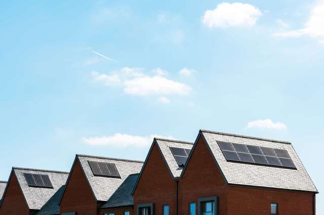 Rooftops of houses with solar panels against a bright blue sky with a few clouds.
