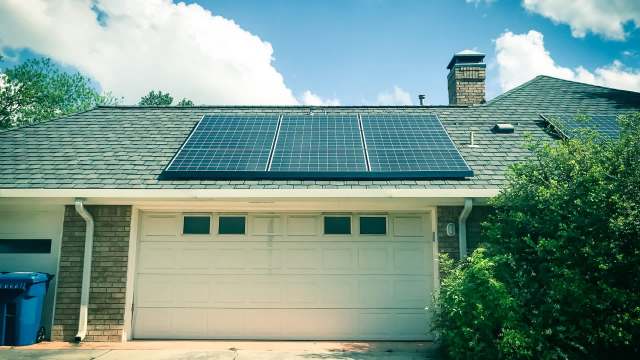 A house with solar panels on the roof and a garage door beneath.