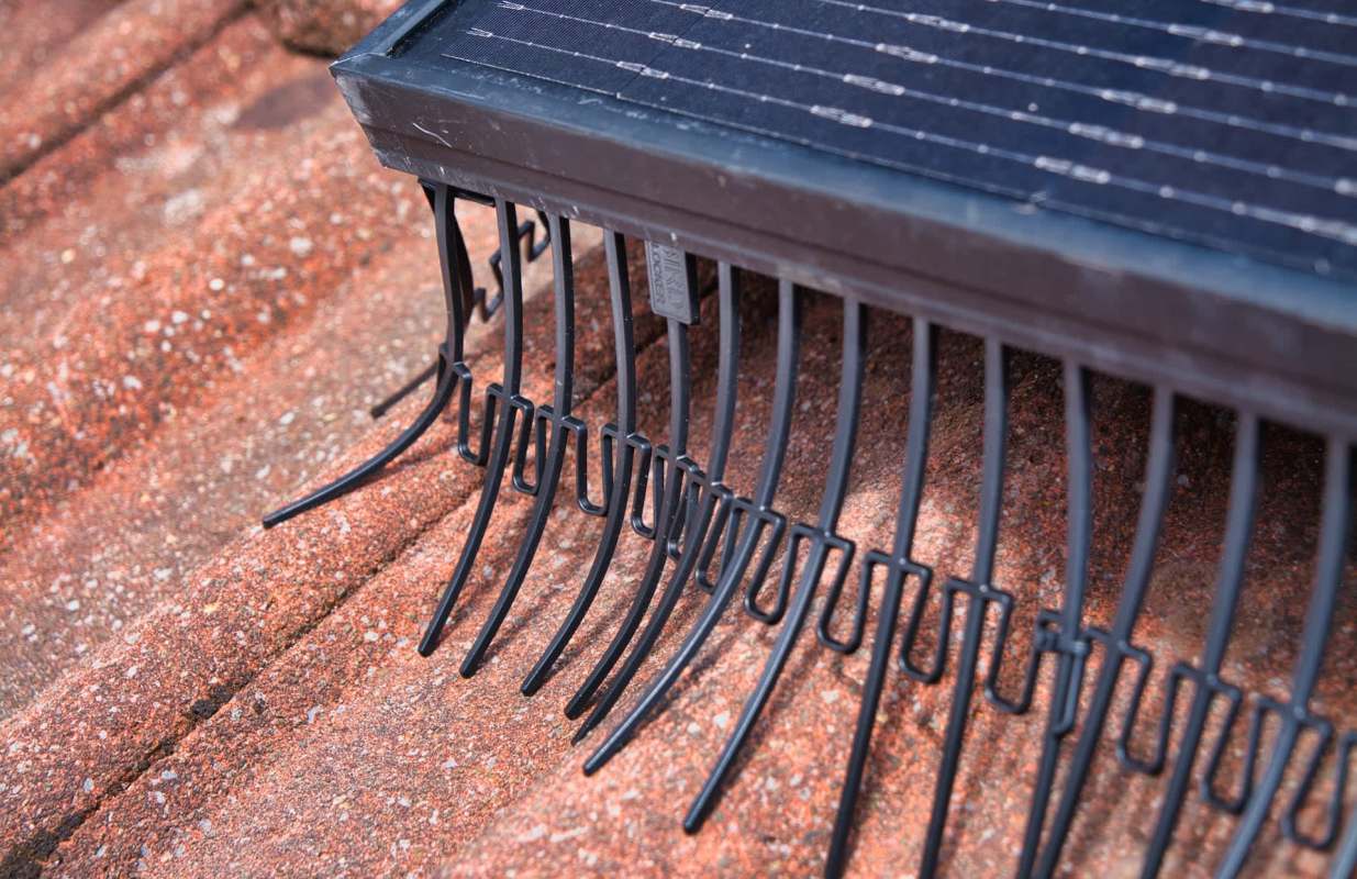 A solar panel with metal hooks is positioned on a textured surface.