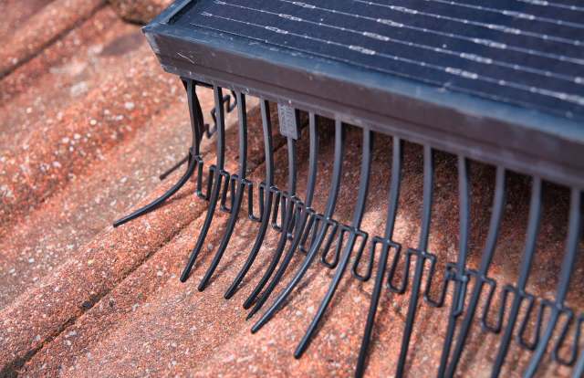 A solar panel with metal hooks is positioned on a textured surface.