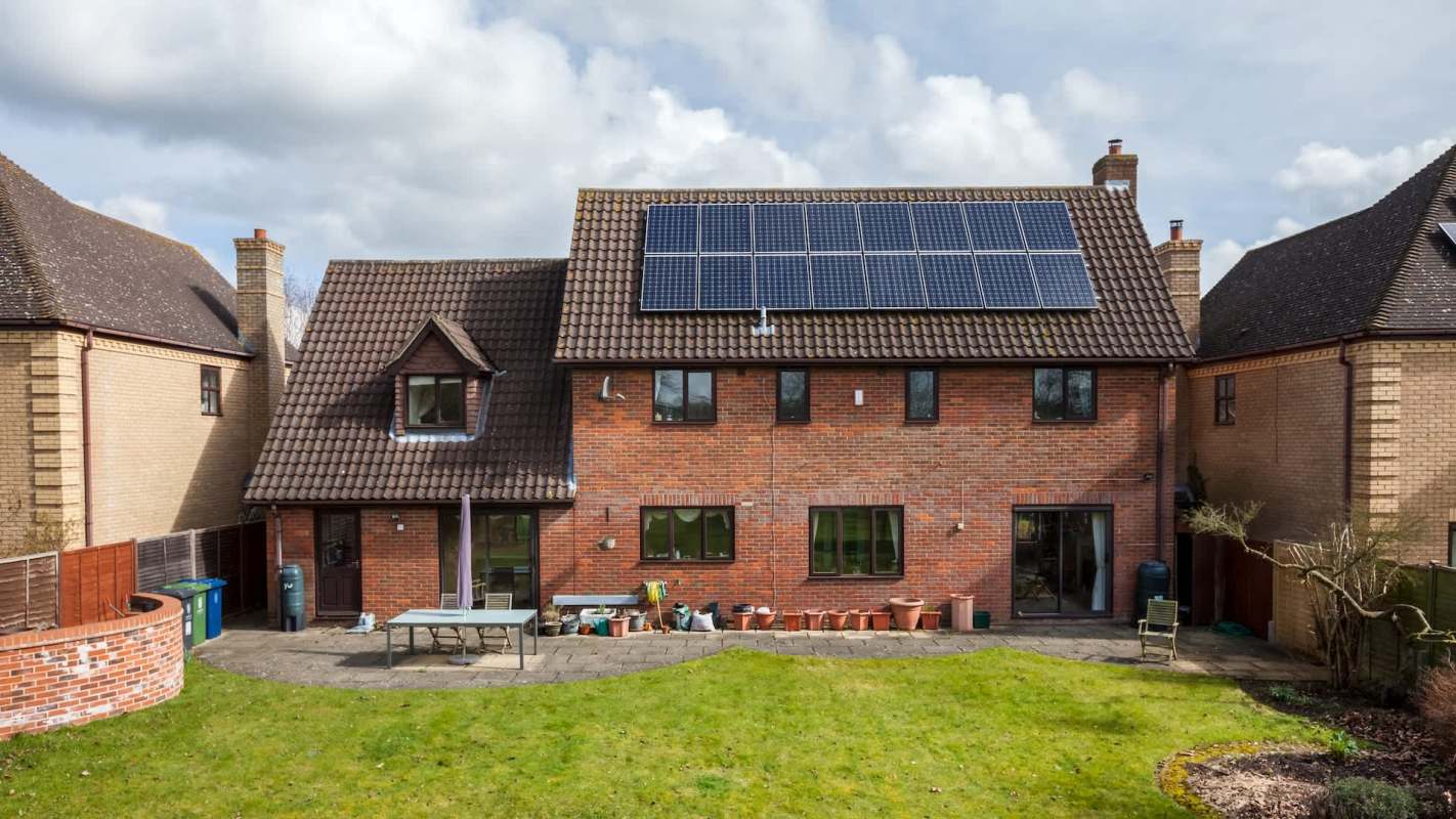 A brick house with solar panels on the roof and a patio surrounded by garden pots.