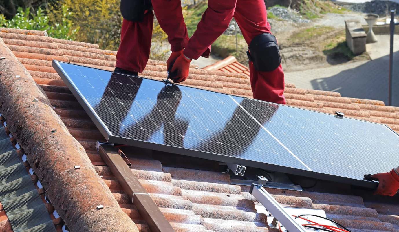 A worker installs a solar panel on a tiled roof.