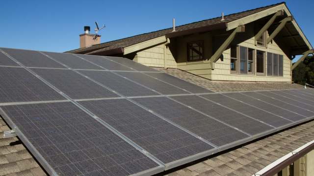 Solar panels installed on a sloped rooftop of a house under a clear blue sky.