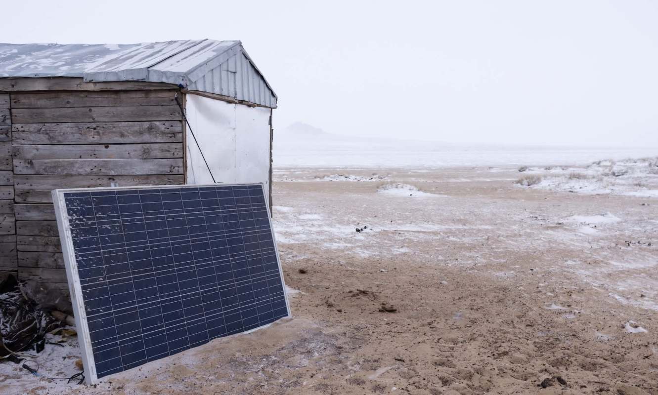 A solar panel is placed next to a small wooden structure in a snowy, cloudy landscape.