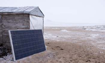 A solar panel is placed next to a small wooden structure in a snowy, cloudy landscape.