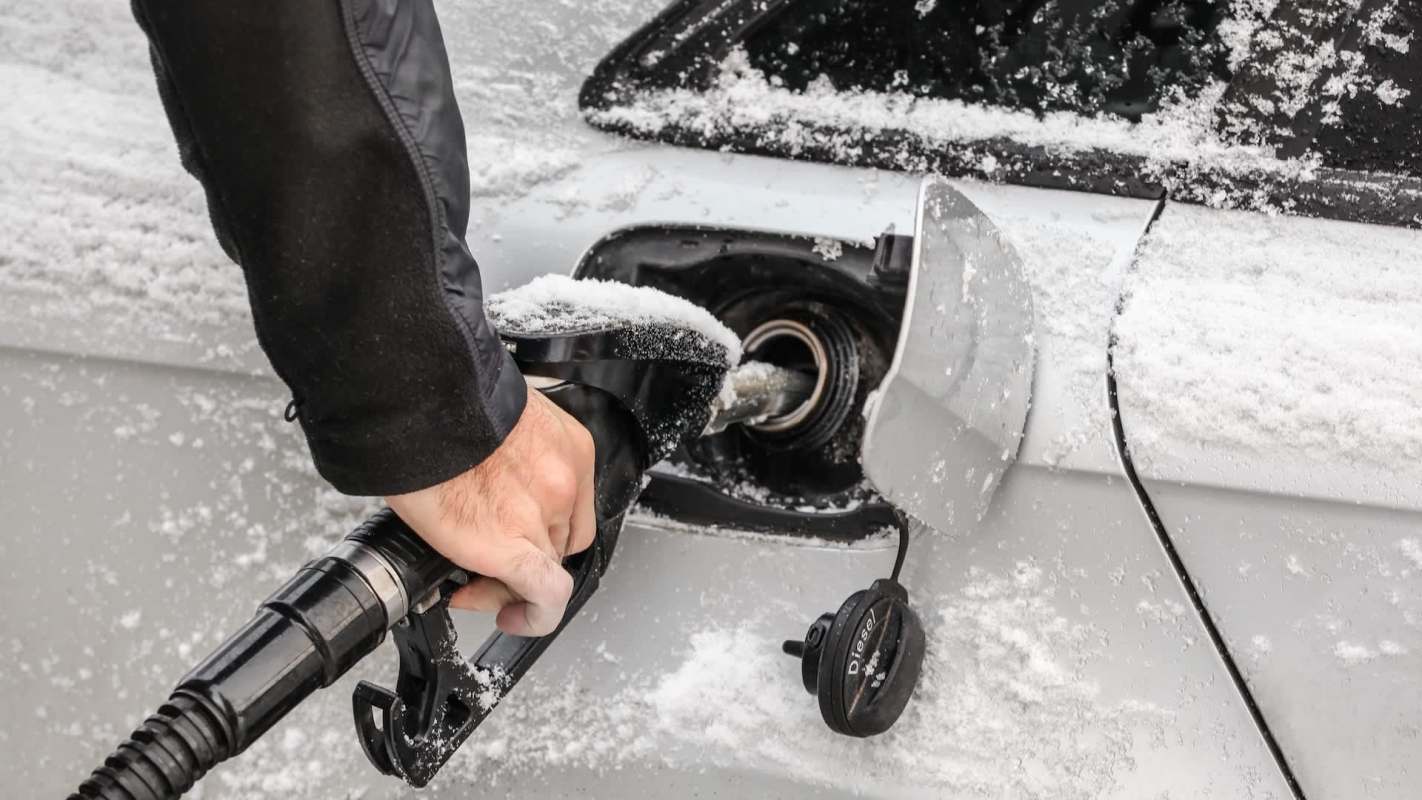 A person fueling a vehicle covered in snow.