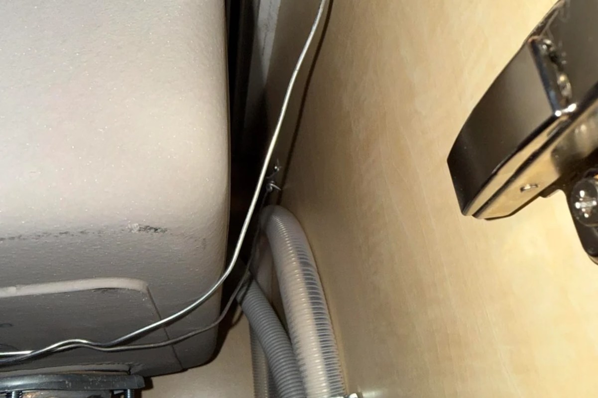 A close-up view of plumbing connections and wires against a wooden surface.