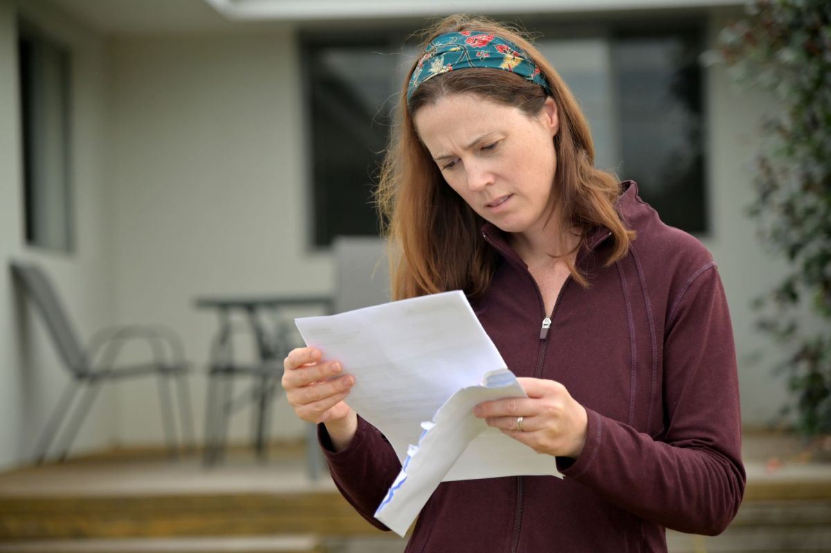 A woman reading a document outside near a table and chairs.