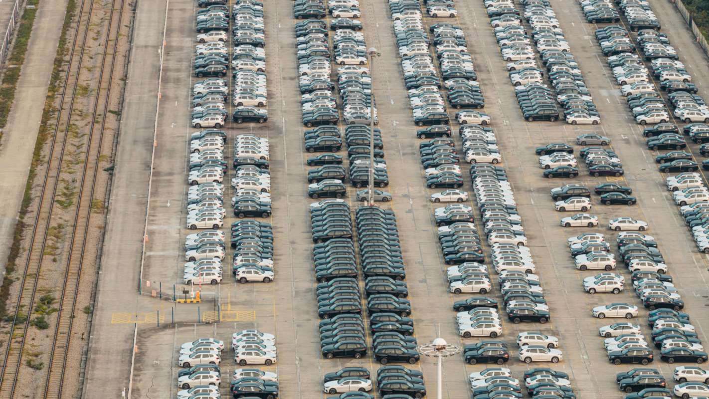 Aerial view of a large parking lot filled with rows of cars and adjacent train tracks.