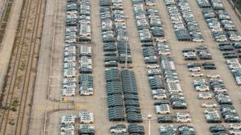 Aerial view of a large parking lot filled with rows of cars and adjacent train tracks.