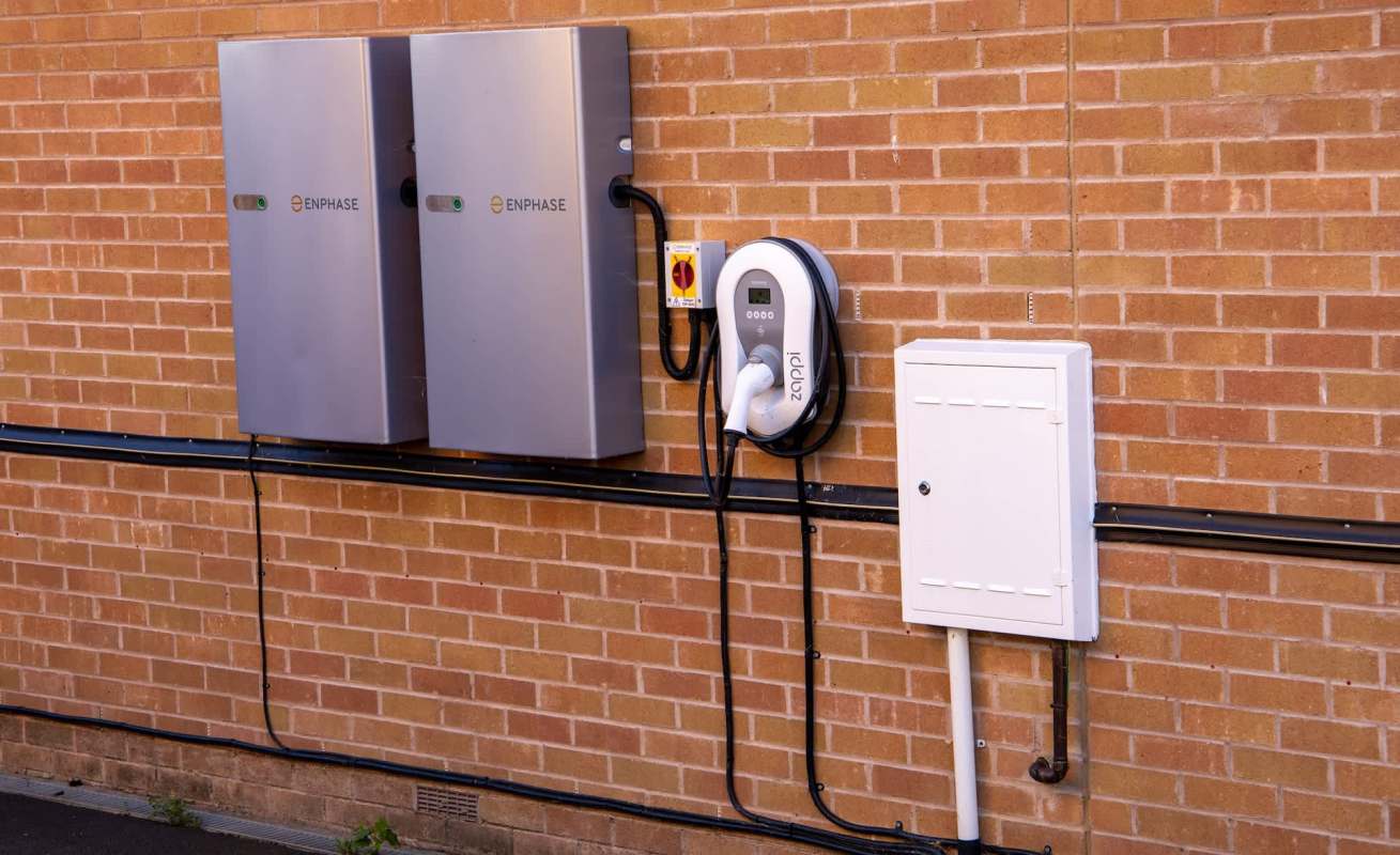Two gray Enphase energy storage units and an electric vehicle charging station mounted on a brick wall.