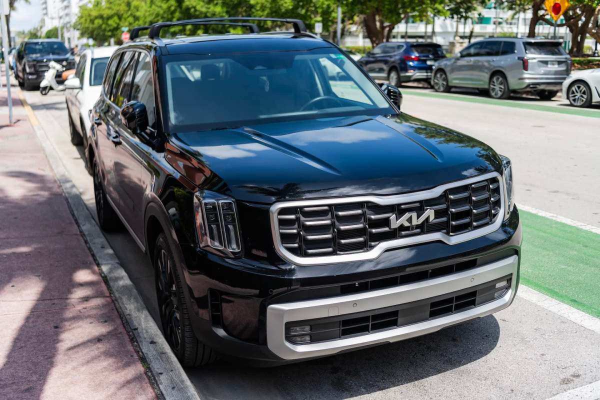 A black Kia SUV parked along a city street with other vehicles in the background.