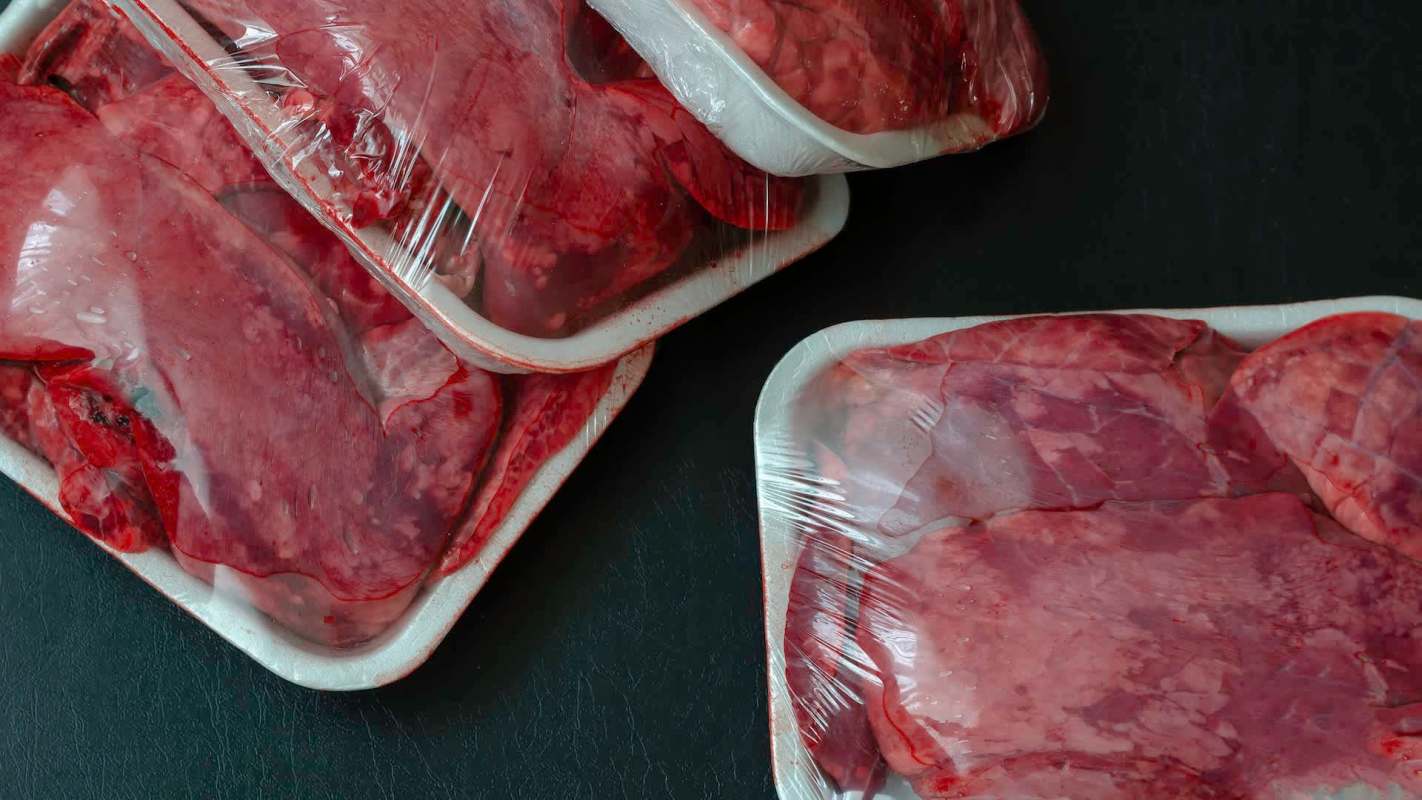 Various packages of raw meat wrapped in plastic, arranged on a dark surface.