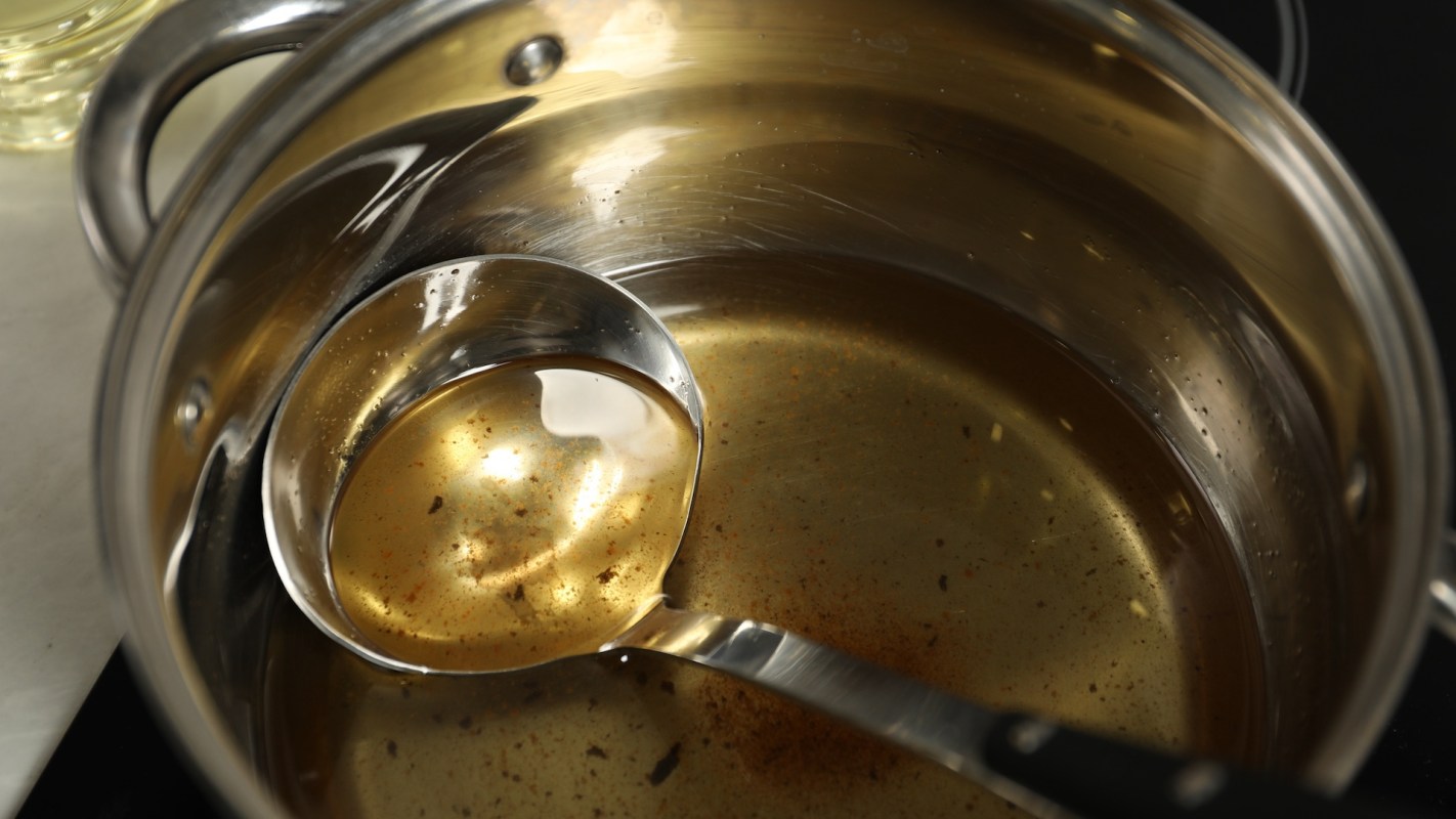 A metallic pot containing oil and a ladle resting inside.
