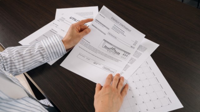 A person reviews an energy statement among various documents on a table.