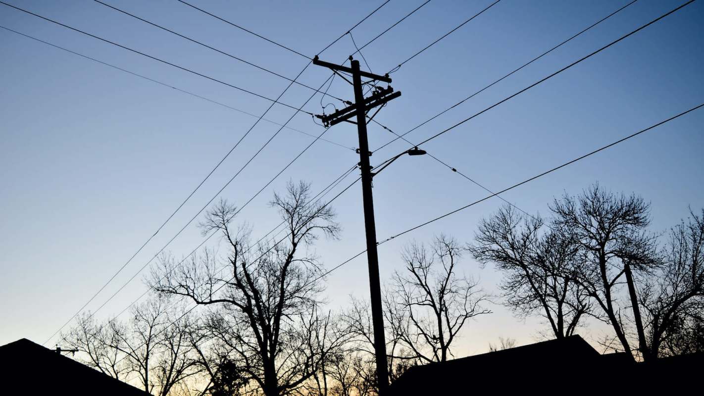 A power pole and bare trees silhouetted against a gradient sky at dusk.