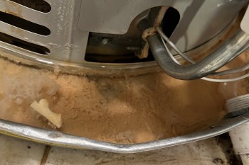 A close-up of a gray water heater with rust and sediment buildup around its base.