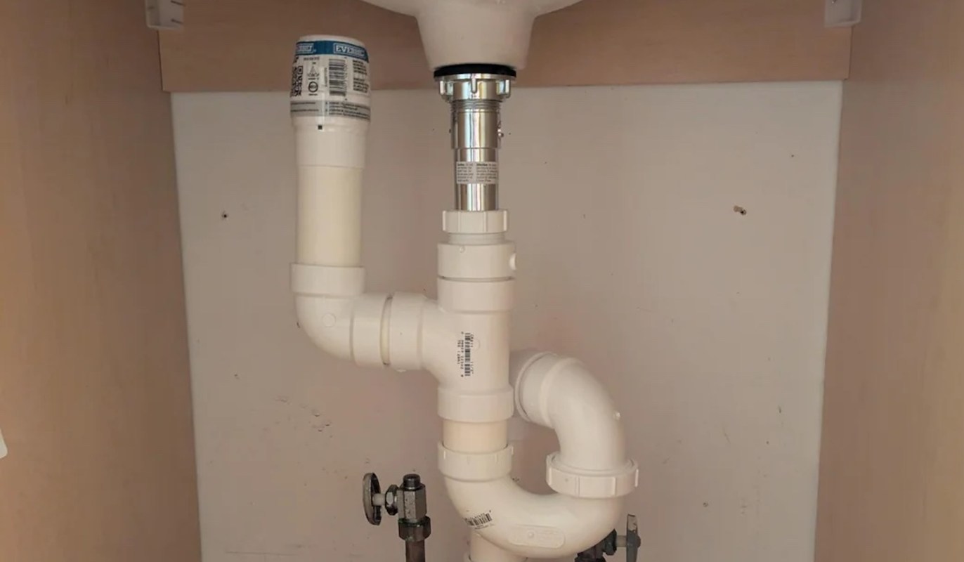 A plumbing setup under a sink featuring PVC pipes and a water shutoff valve.
