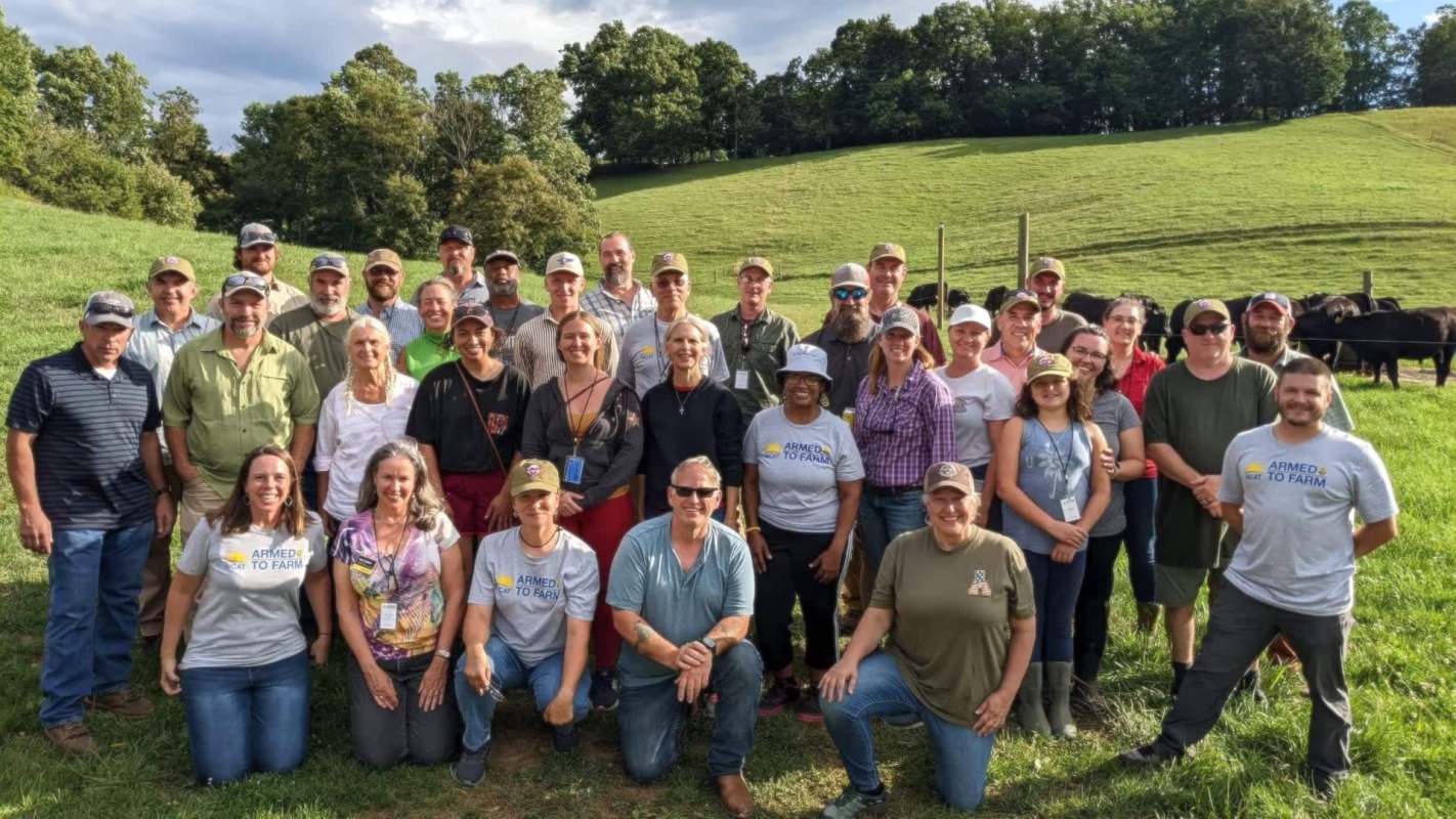 A group of people poses for a photo in a green field with cows in the background.