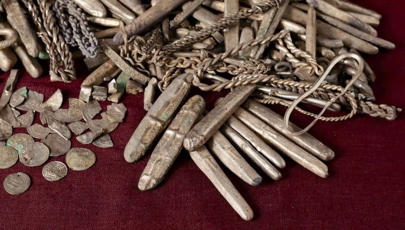 A collection of ancient silver coins and decorative metal pieces on a dark fabric surface.