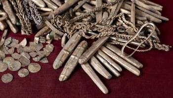 A collection of ancient silver coins and decorative metal pieces on a dark fabric surface.