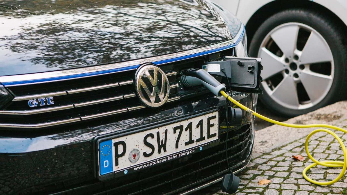 A black Volkswagen electric car is plugged into a charging station on a cobblestone street.