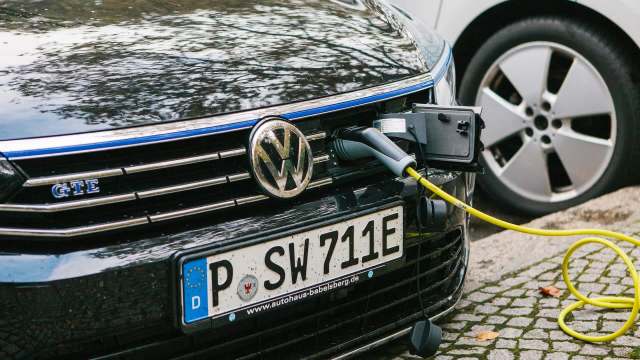 A black Volkswagen electric car is plugged into a charging station on a cobblestone street.