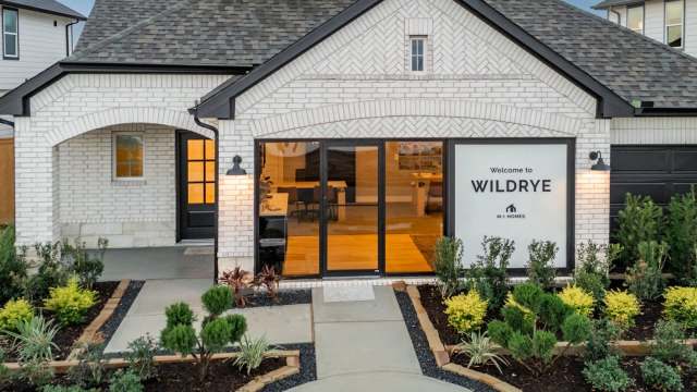 A modern house exterior with a welcome sign, landscaped garden, and large windows.