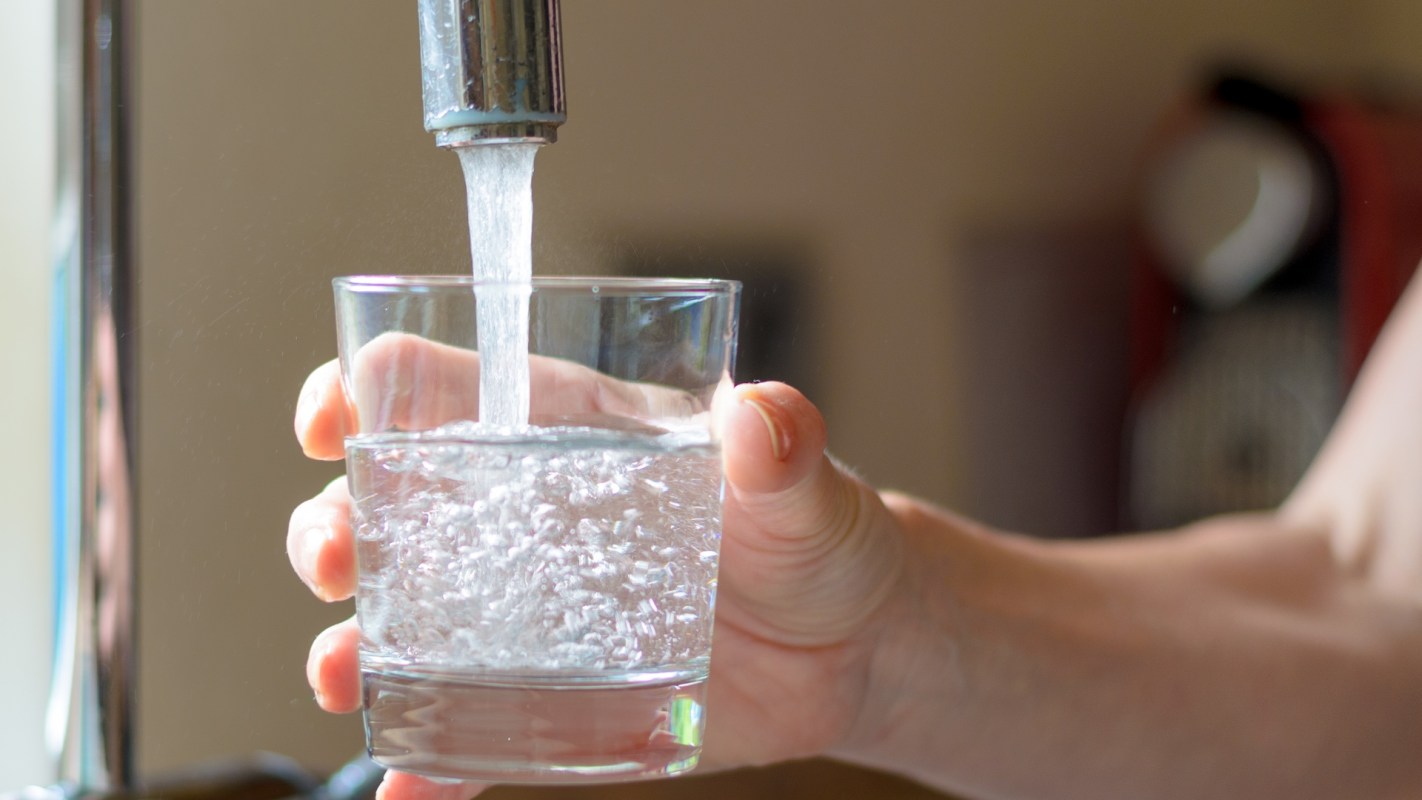 A hand holds a glass as water flows from a tap into it.