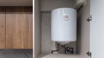A white water heater installed in a cabinet with visible plumbing connections.